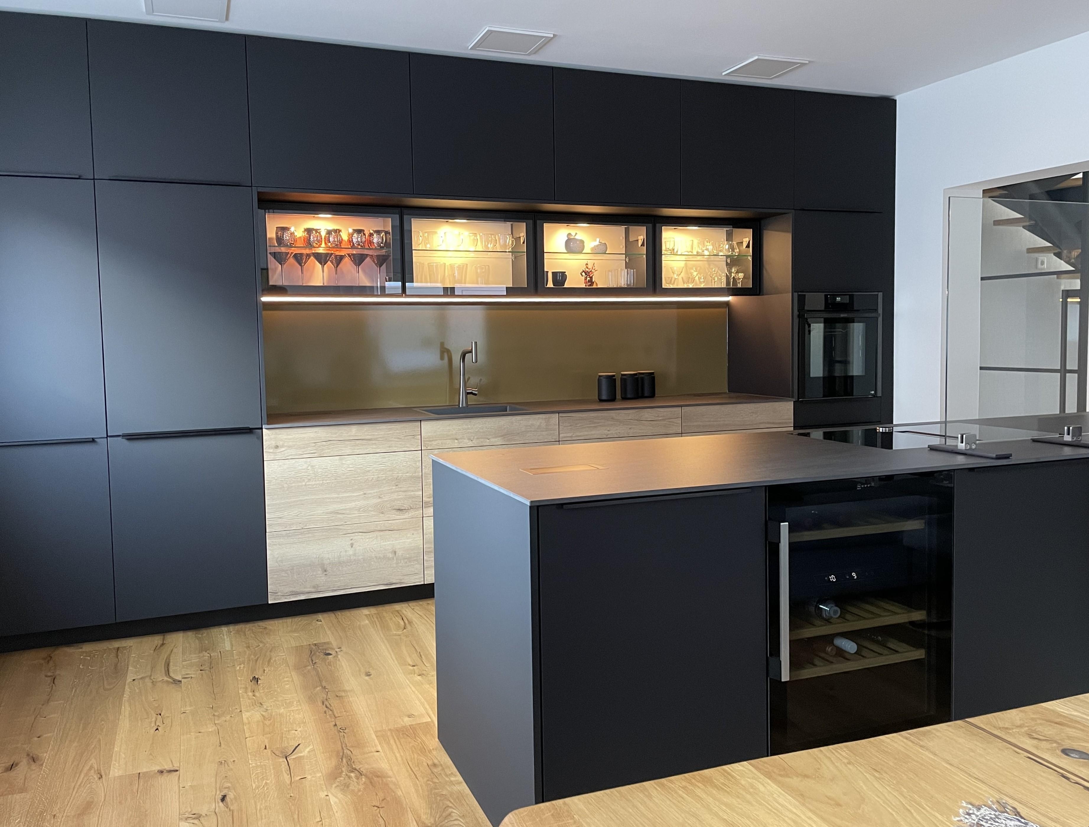 Moderne Küche mit dunklen Schränken, Holzarbeitsplatte und beleuchteten Vitrinen.