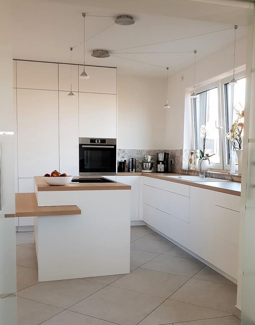 Moderne, helle Küche mit Kochinsel, weißen Schränken und großem Fenster