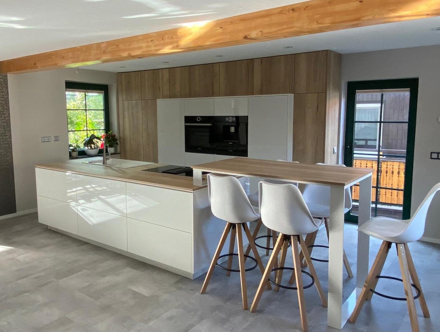 Moderne Küche mit weißen Schränken, Holztheke und drei weißen Barhockern