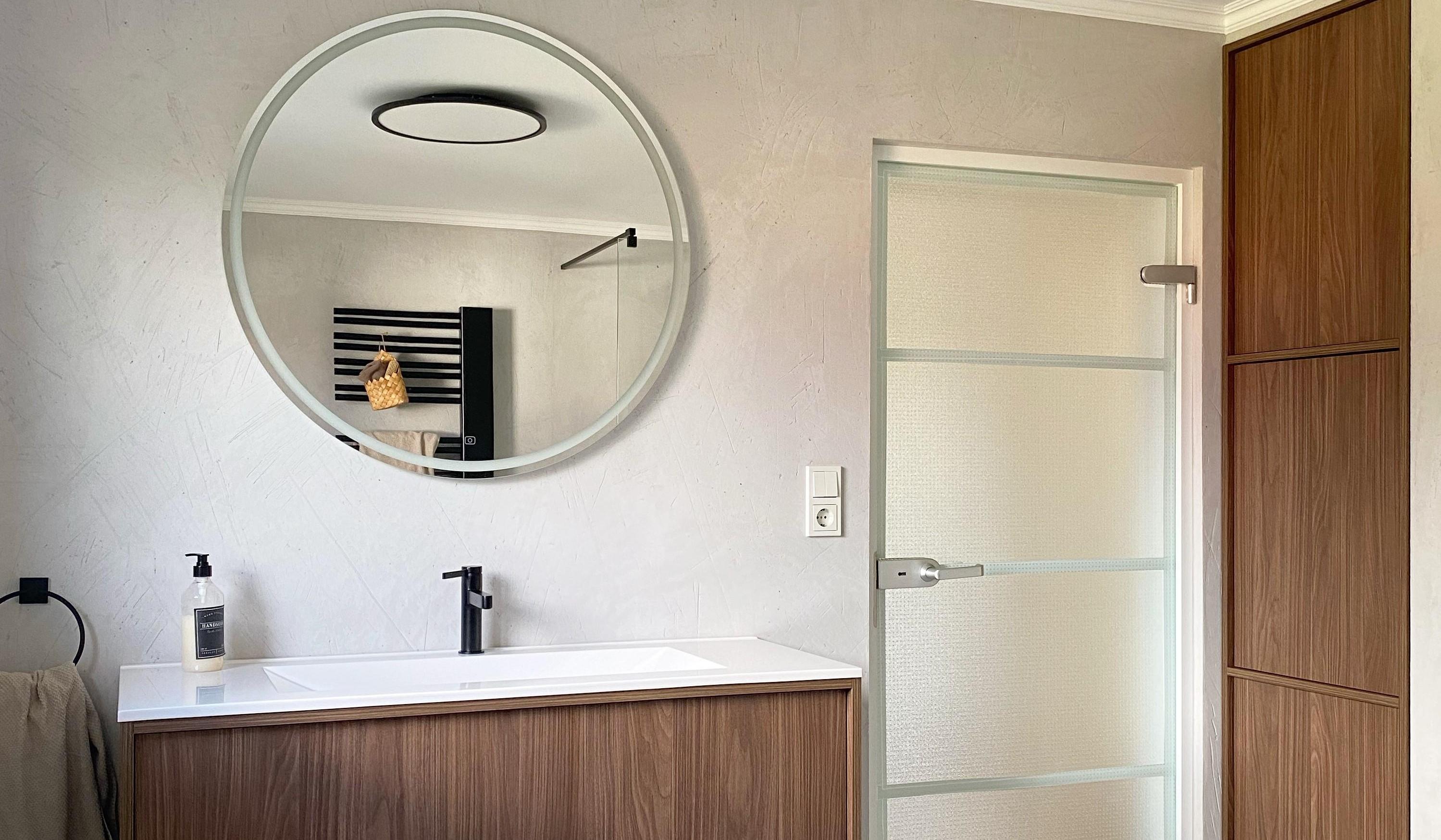 Bad mit Waschtisch und rundem Spiegel darüber. 