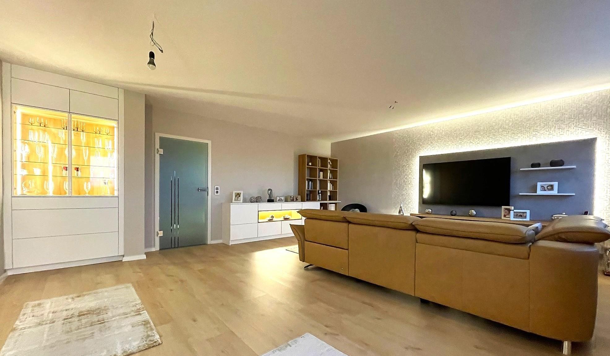 Wohnzimmer mit Couch und Fernsehwand recht und Vitrine auf der linken Seite.