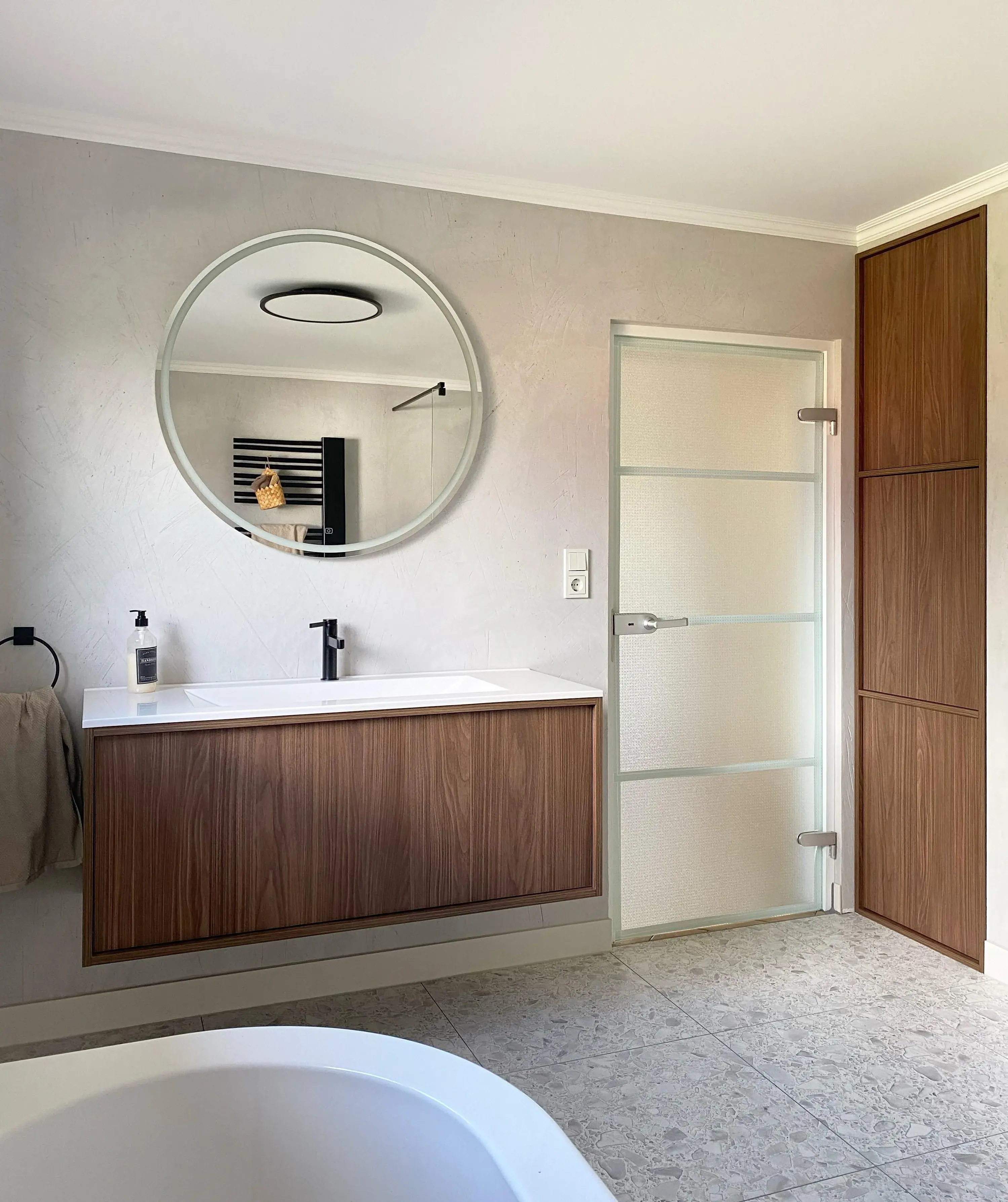 Bad mit Waschtisch und rundem Spiegel darüber. 