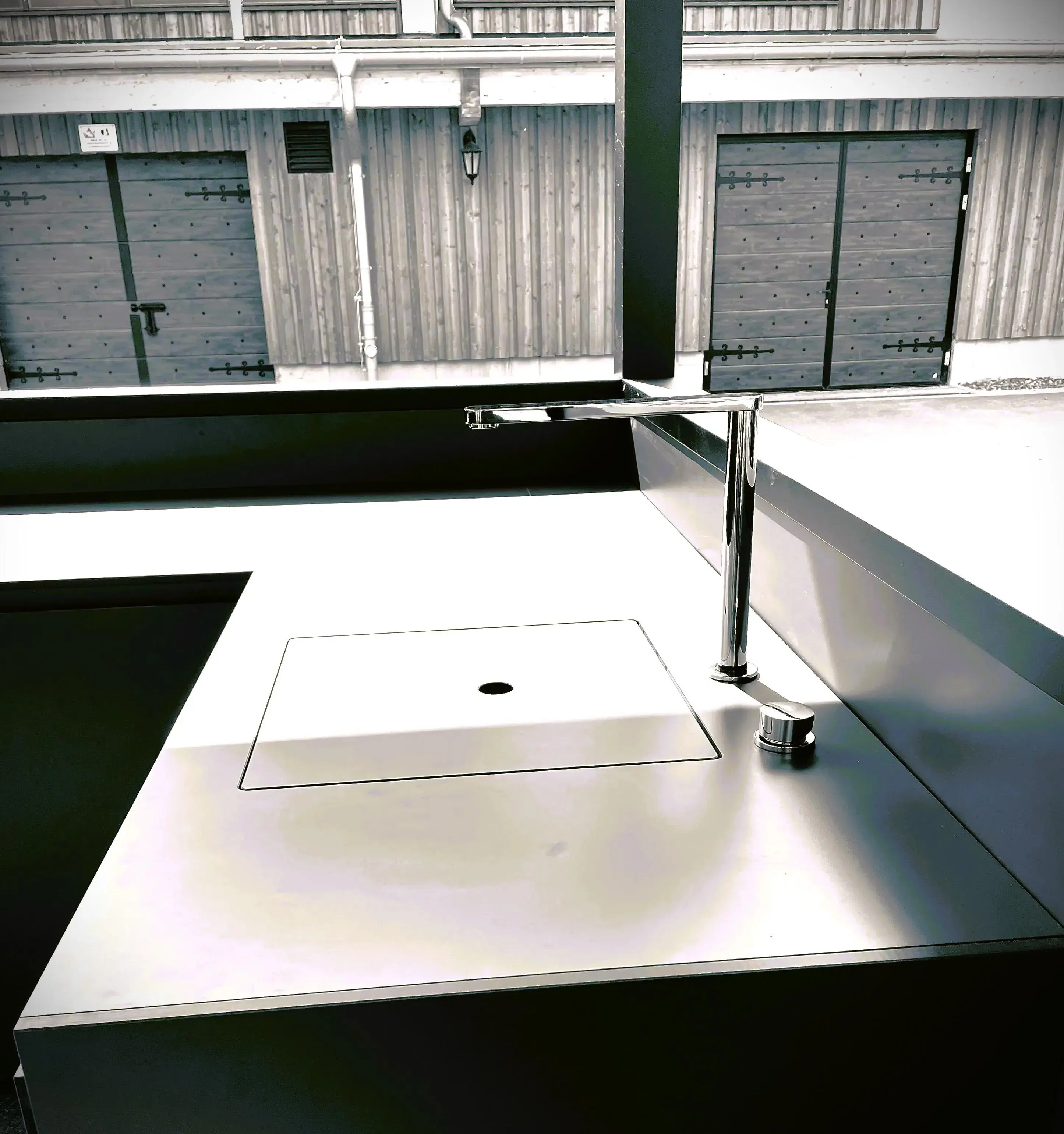 Moderne Edelstahlspüle mit Wasserhahn vor Holzwand und Garagentoren.