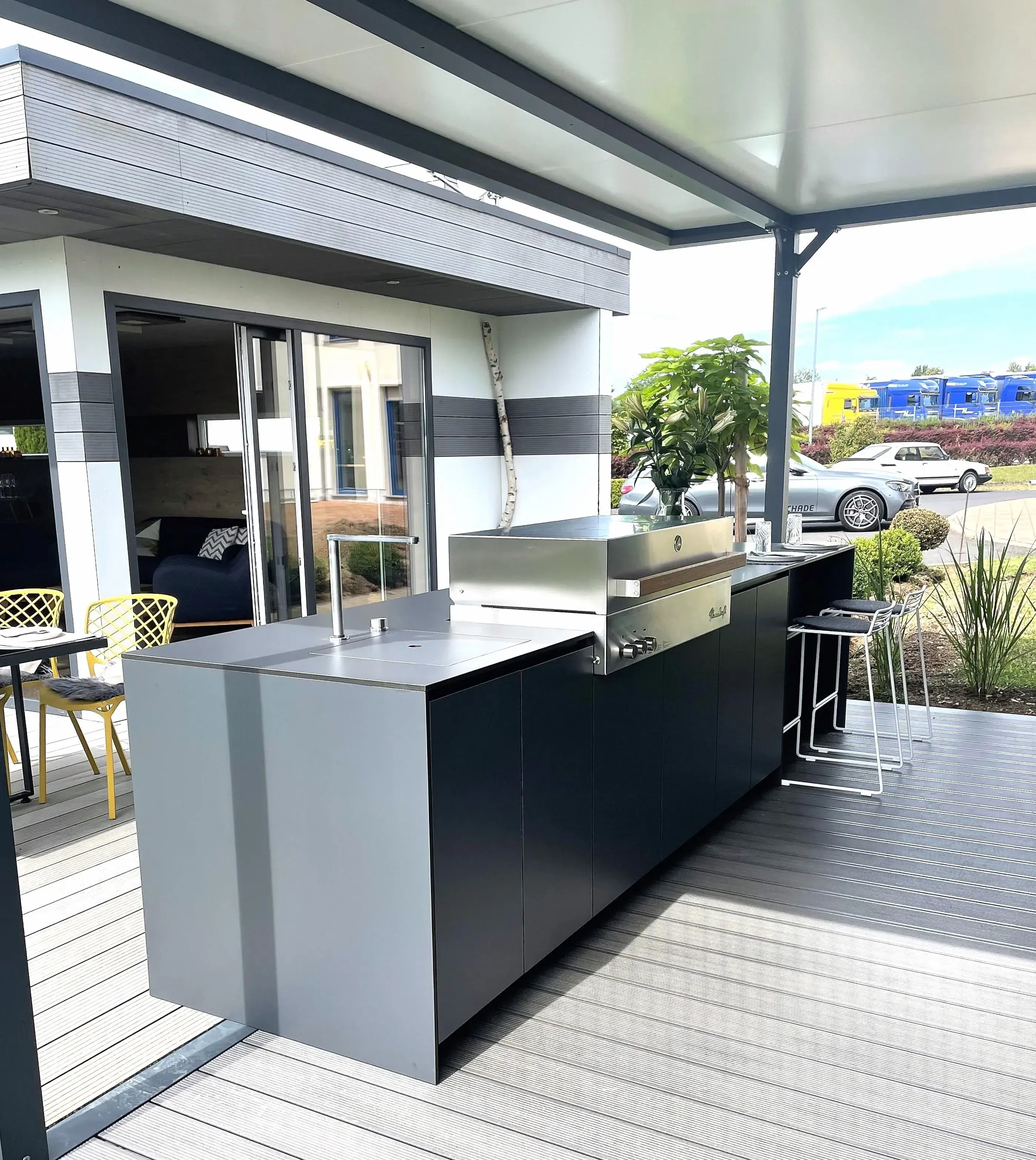 Moderne Outdoorküche mit Grill und Sitzgelegenheiten auf einer überdachten Terrasse.