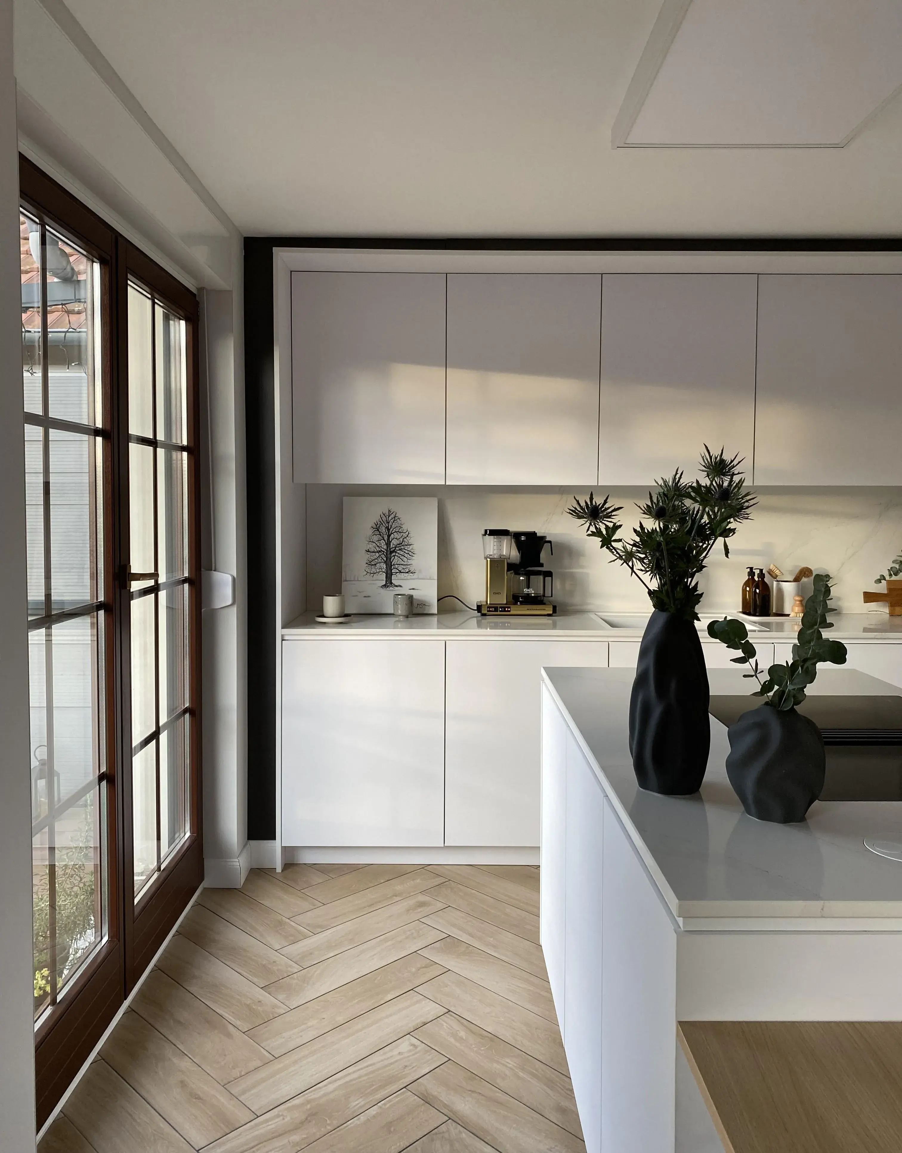 Moderne helle Küche mit weißen Schränken, Holzfußboden und Vasen mit Pflanzen.