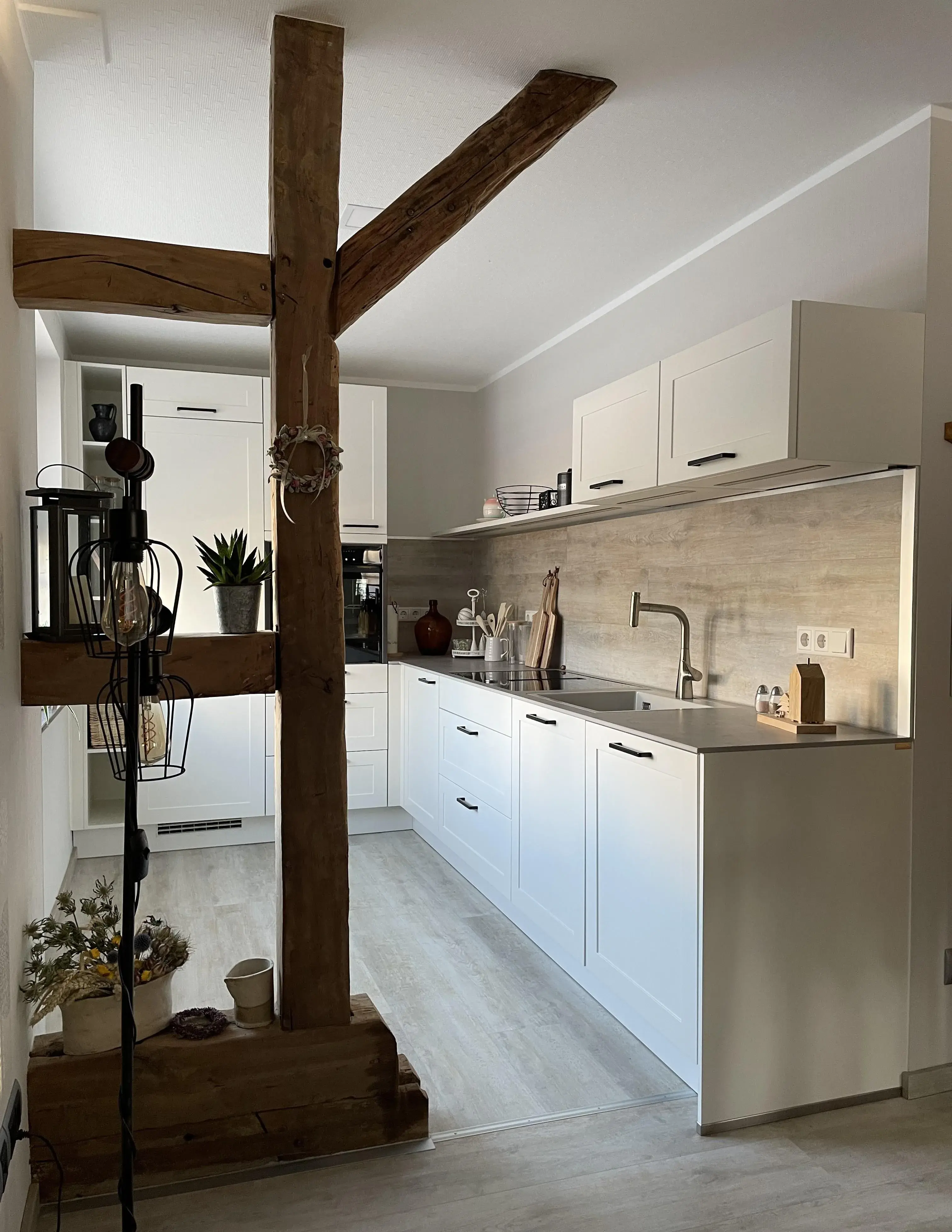 Moderne weiße Küche mit Holzbalken, Pflanzen und Holzdekor.