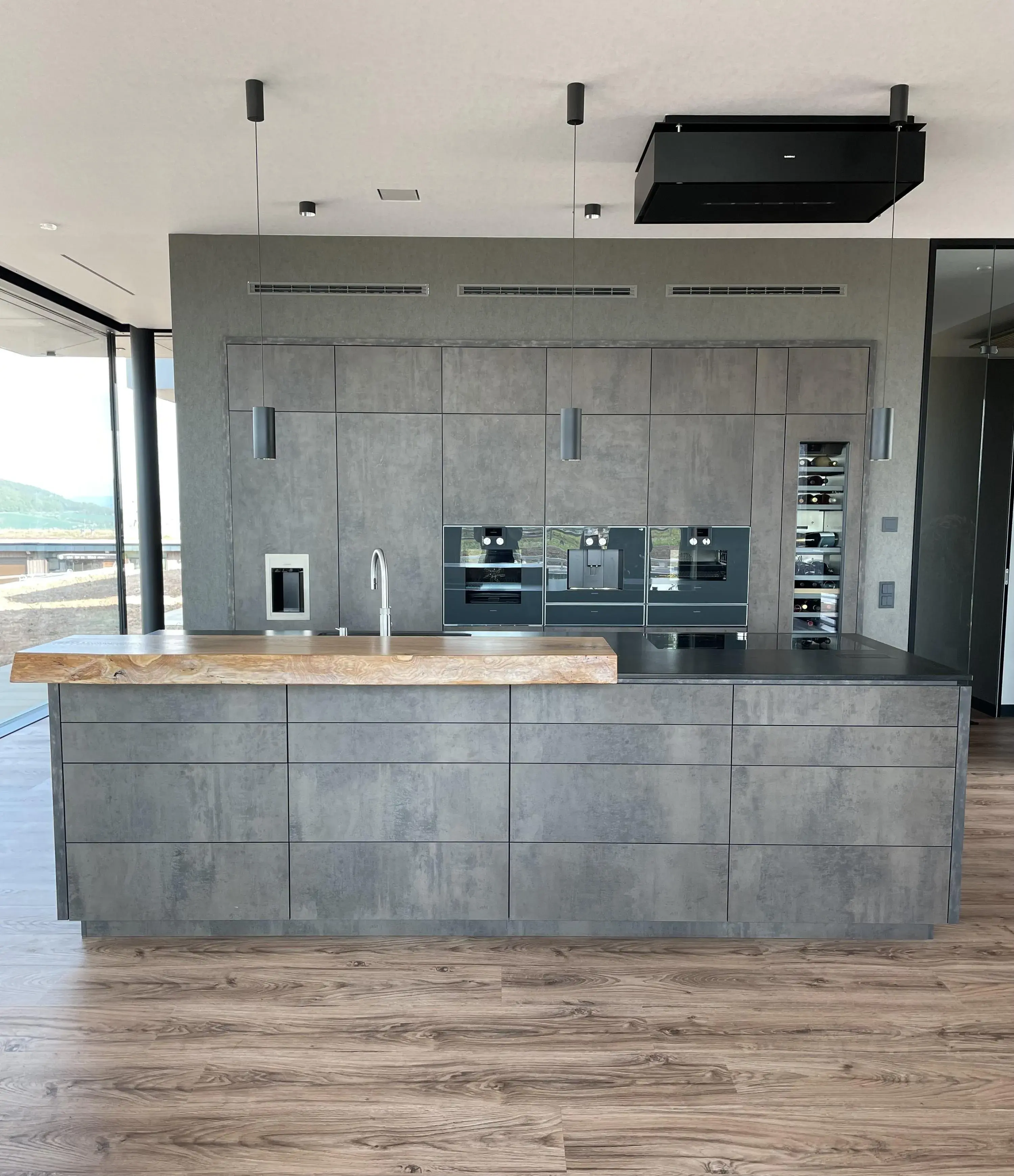 Moderne graue Küche mit Holzboden, großer Insel und eingebauten Geräten.