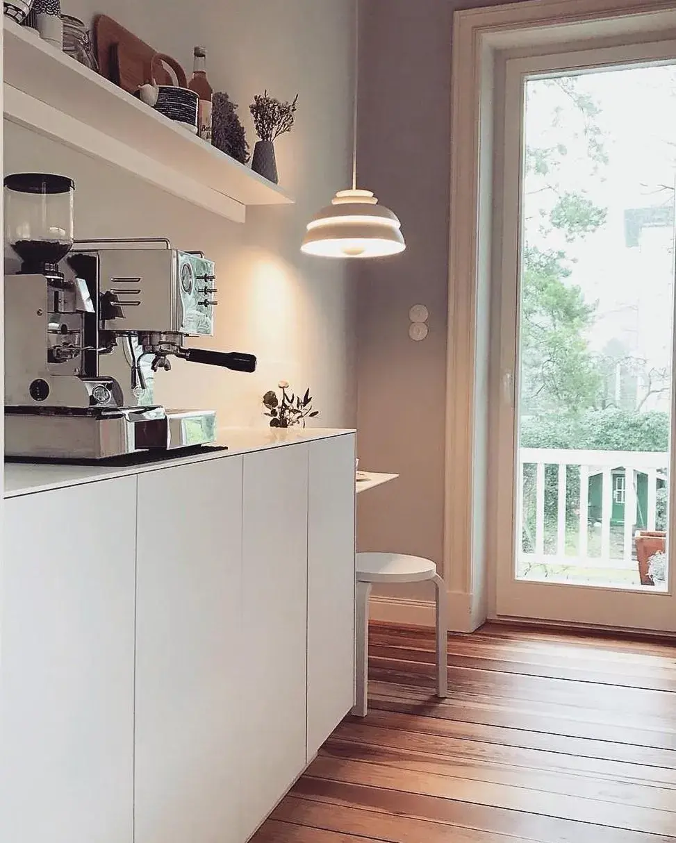 Helle Küche mit Kaffeemaschine, Holzfußboden und großem Fenster zum Balkon.