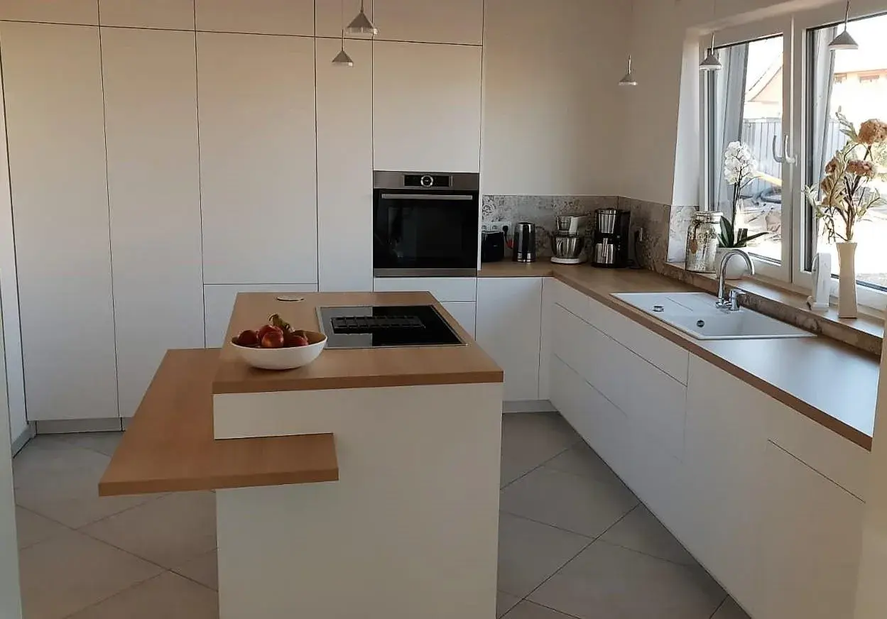 Moderne weiße Küche mit Holzarbeitsplatte und Obstschale auf der Kochinsel.