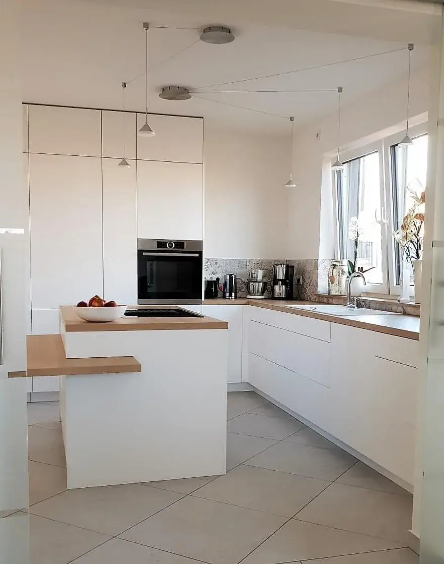 Moderne, helle Küche mit Kochinsel, weißen Schränken und großem Fenster