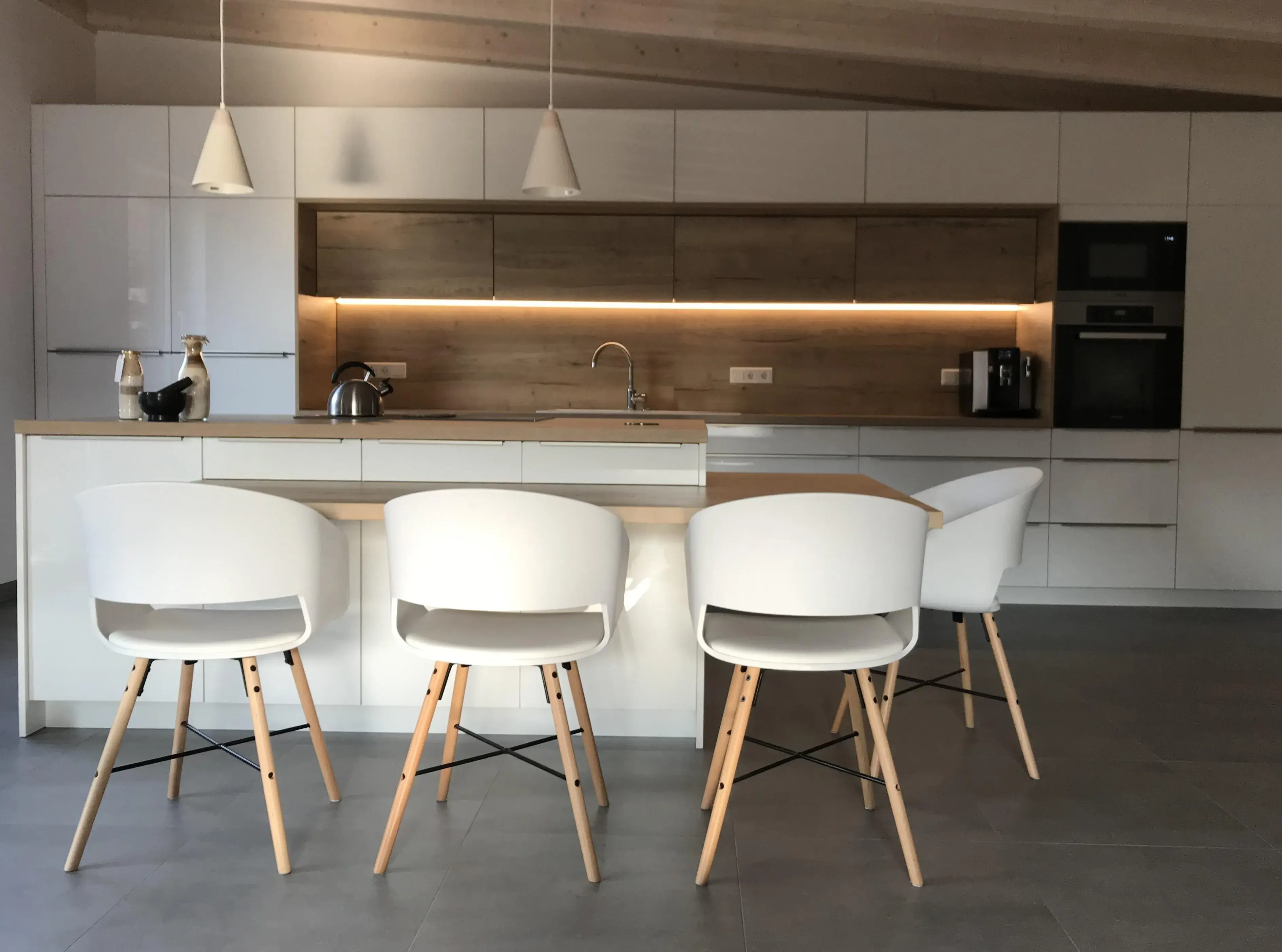 Moderne Küche mit weißer Kochinsel, vier Stühlen und Holzdetails.