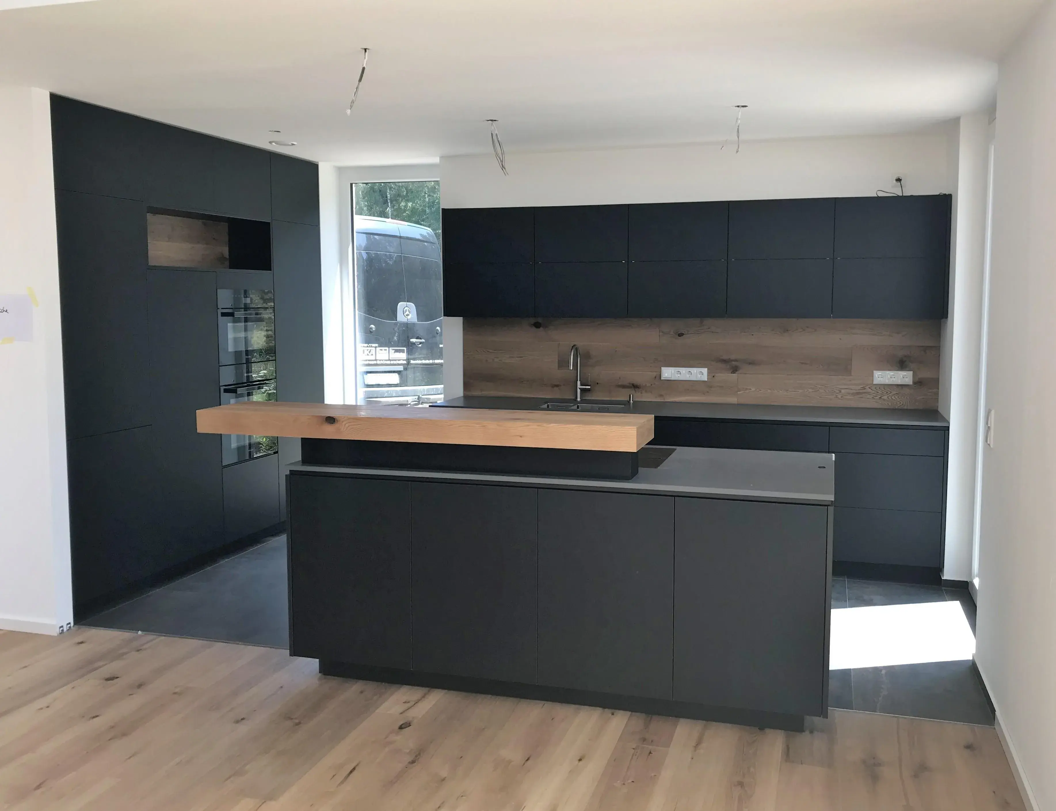 Moderne schwarze Küche mit Holzarbeitsplatte und Kücheninsel, viel Tageslicht