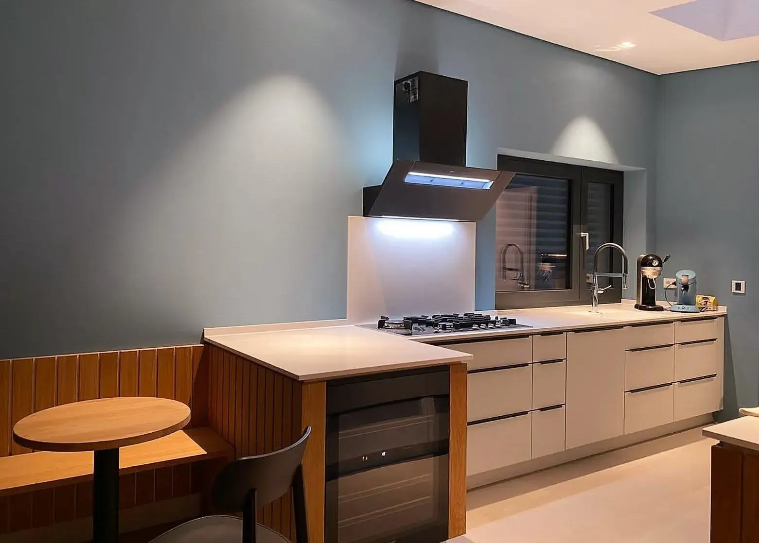 Moderne Küche mit grauen Schränken, Kochfeld, Dunstabzugshaube und kleinem Essbereich