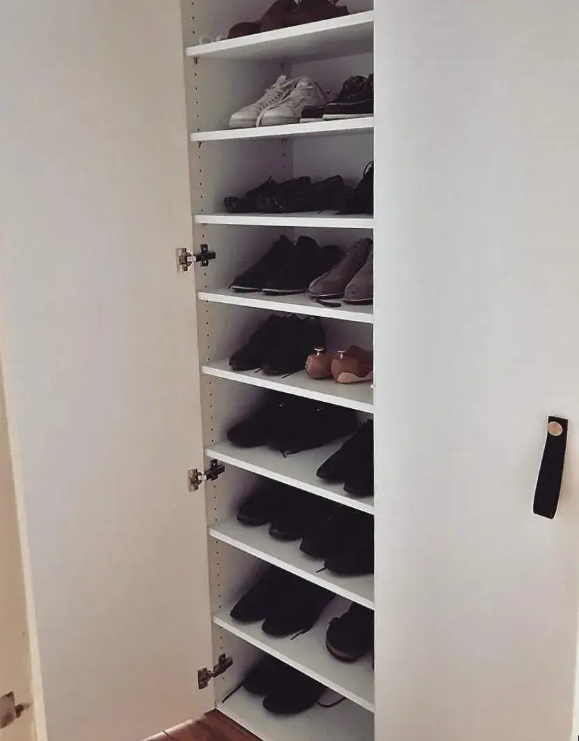 Schrankwand, bei der eine Tür geöffnet ist und hinter der Schuhe aufbewahrt werden. 