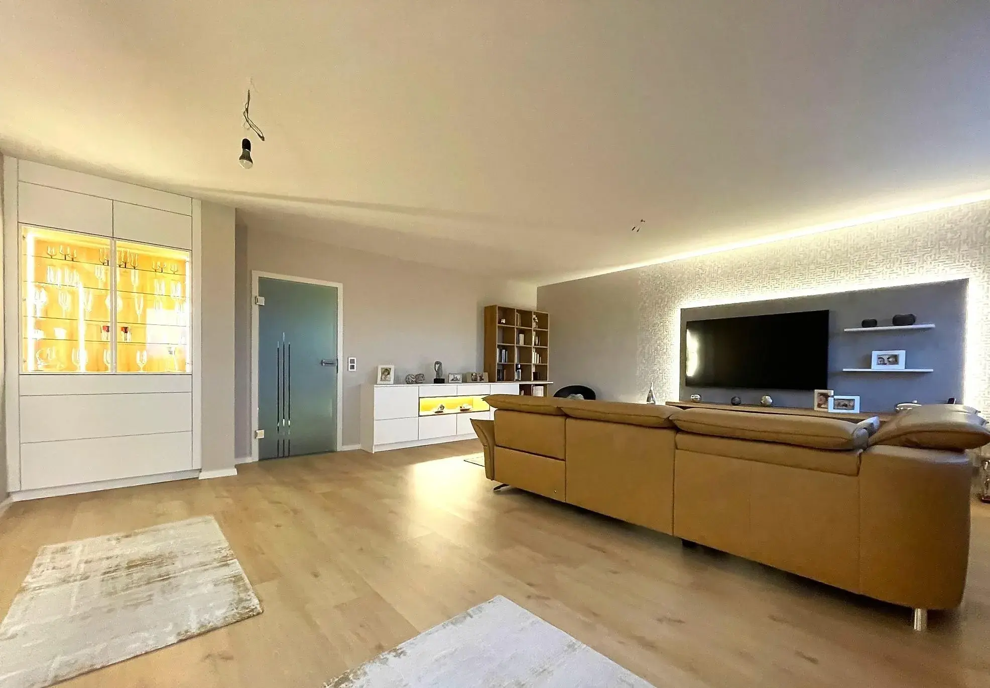 Wohnzimmer mit Couch und Fernsehwand recht und Vitrine auf der linken Seite.